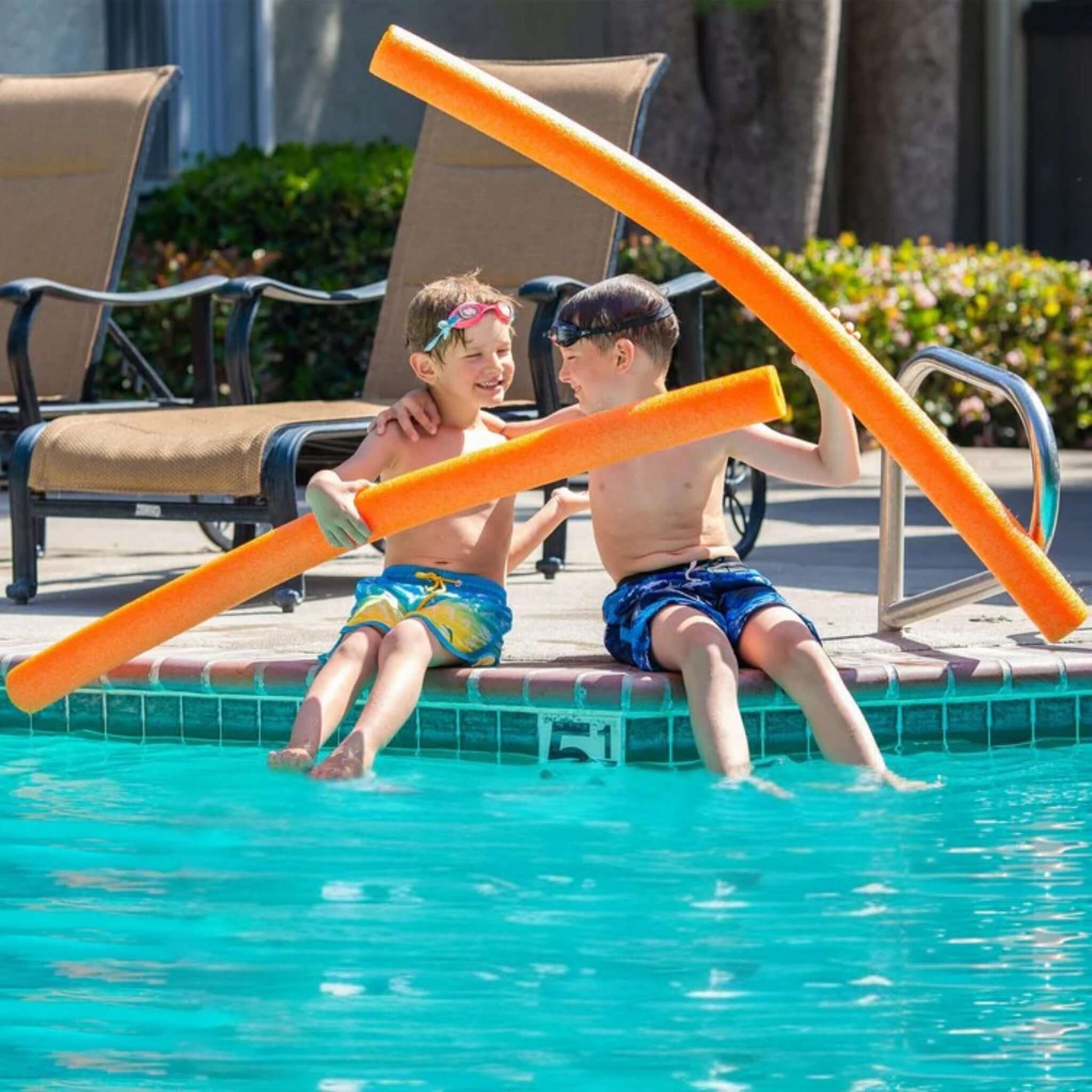 Two kids play with Deluxe Foam Swim Noodles | Orange | Black | Purple | 47" x 2.25" at a poolside, enjoying summer fun. WPM pool supplies.
